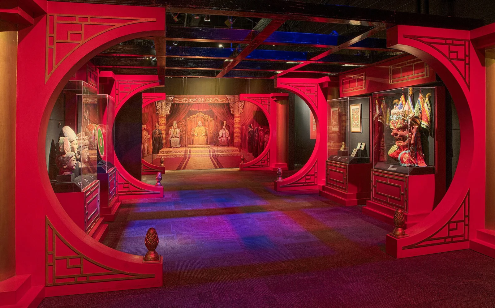 赤い円形の門を模した展示空間に、展示ケース、壁画、衣装を配した「Genghis Khan: Beyond the Empire」の会場風景