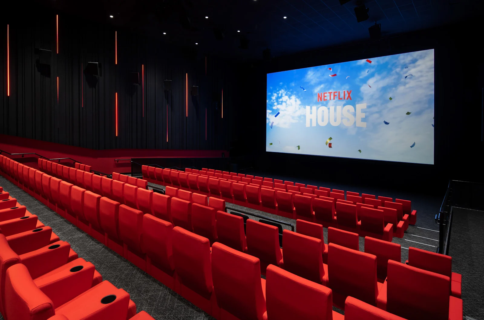 赤い座席と大きなスクリーンを備え、スクリーンにNetflix Houseのロゴが映るTudum Theater内部