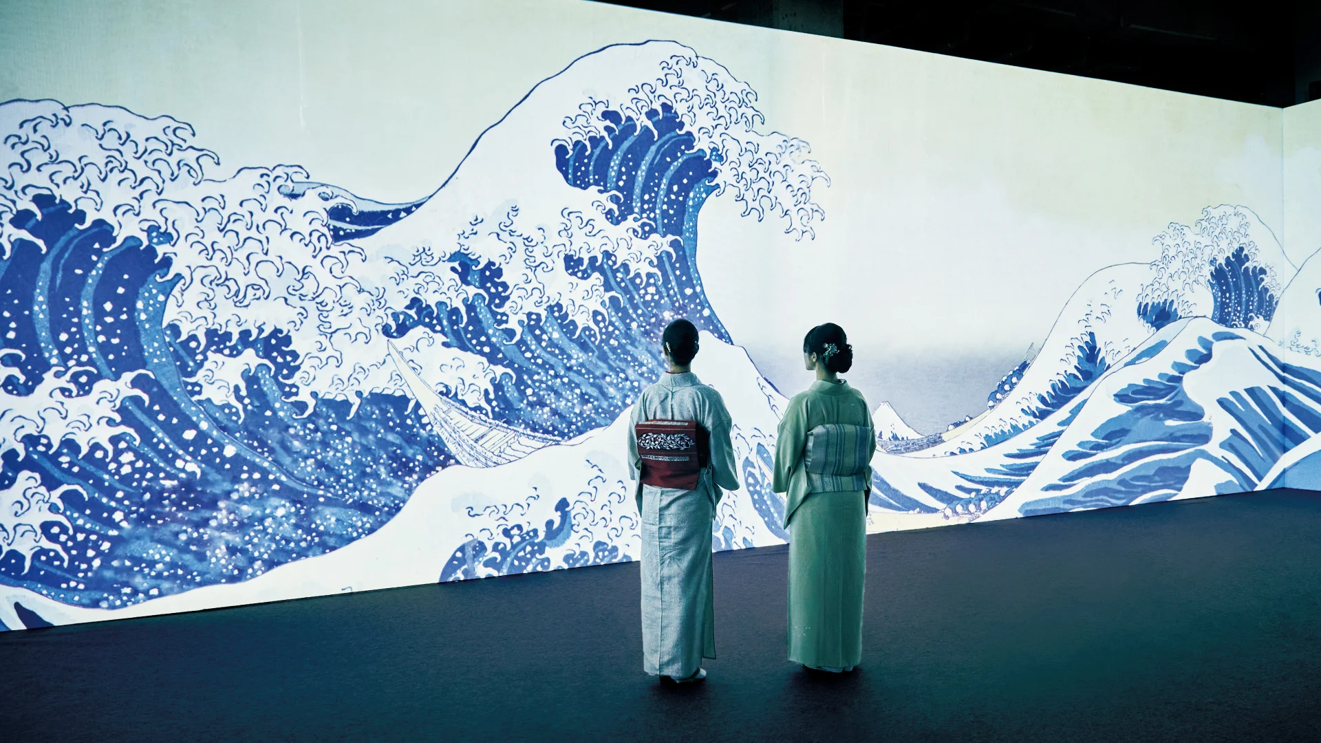 葛飾北斎の神奈川沖浪裏を投影した展示空間に立つ着物姿の来場者2人